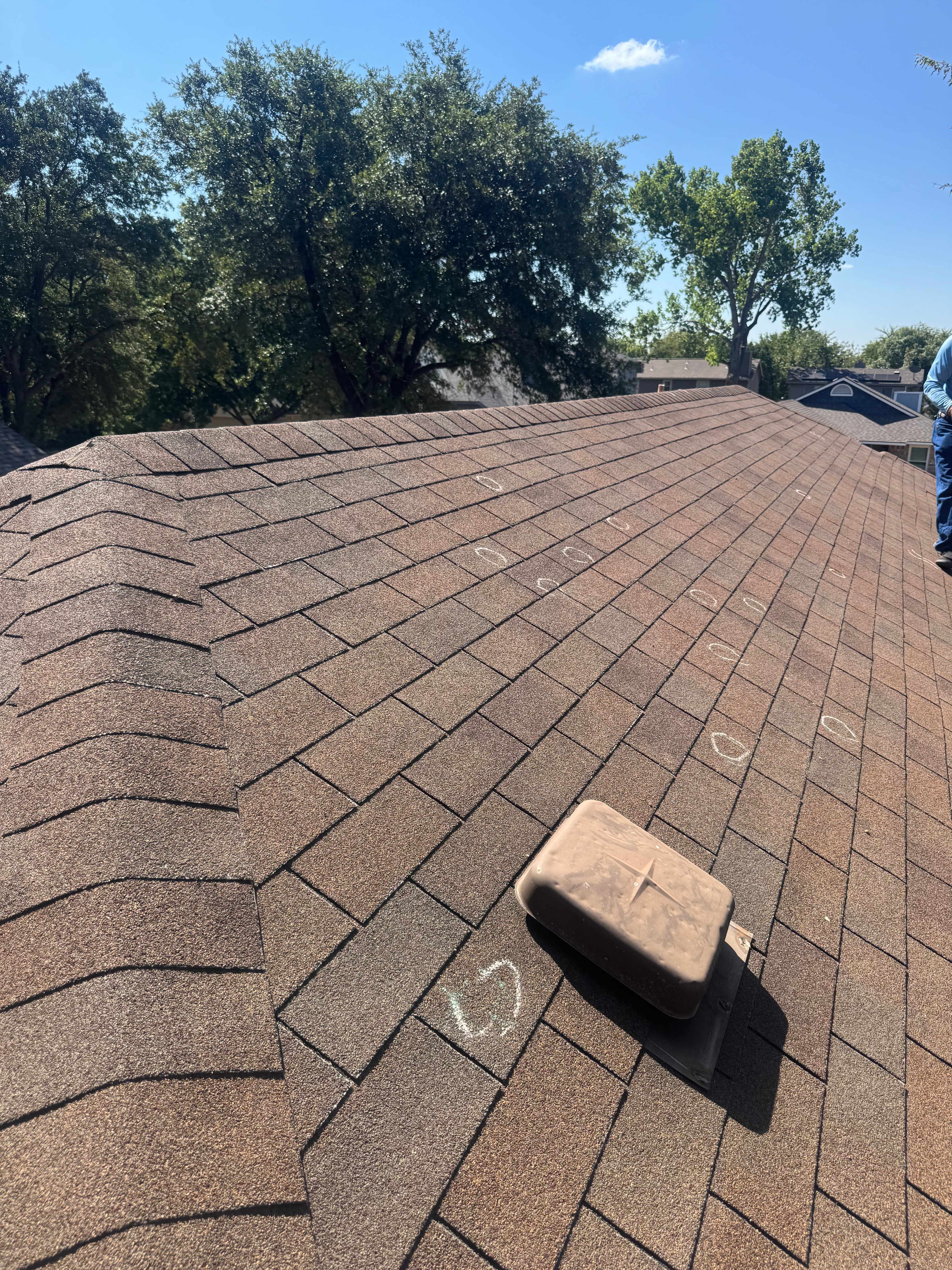 Roof inspection in progress with hail damage circled in white chalk across weathered shingles
